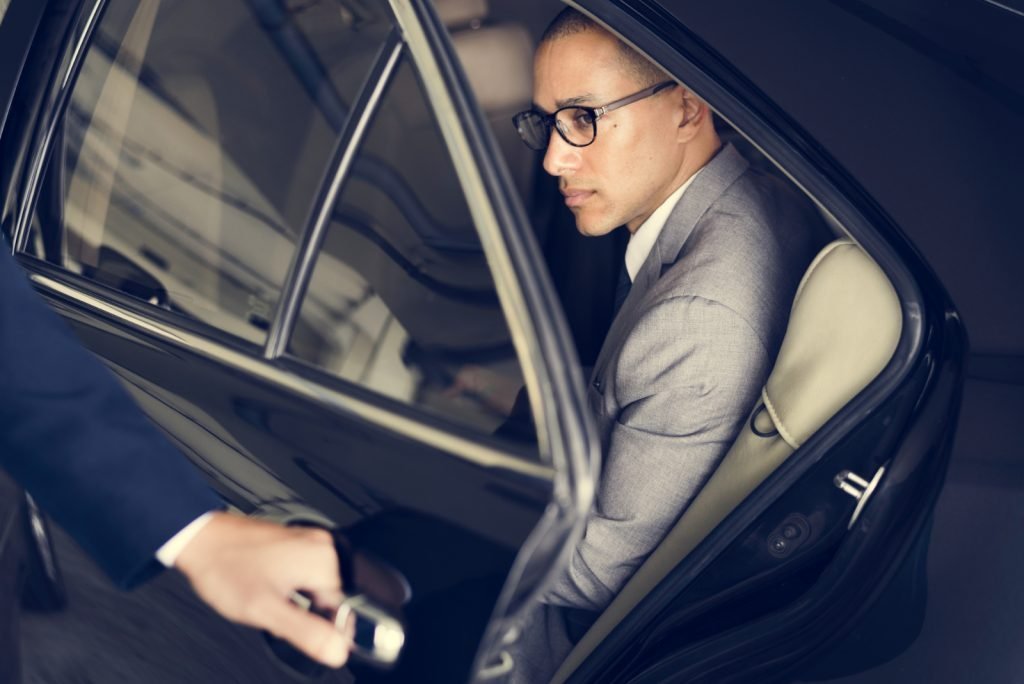 Businessman in a suit sitting in the back seat of a luxury United Limo INC vehicle as a chauffeur opens the door in New York.