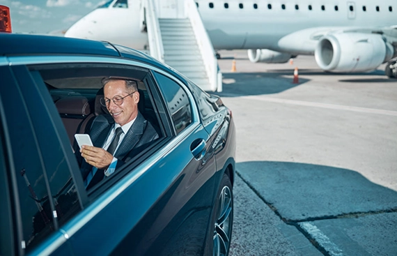 Businessman in a luxury car smiling at phone near private jet at airport – United Limo INC executive airport transfer service.