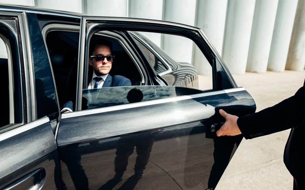 Businessman in suit with sunglasses in luxury black car – United Limo INC executive chauffeur service.